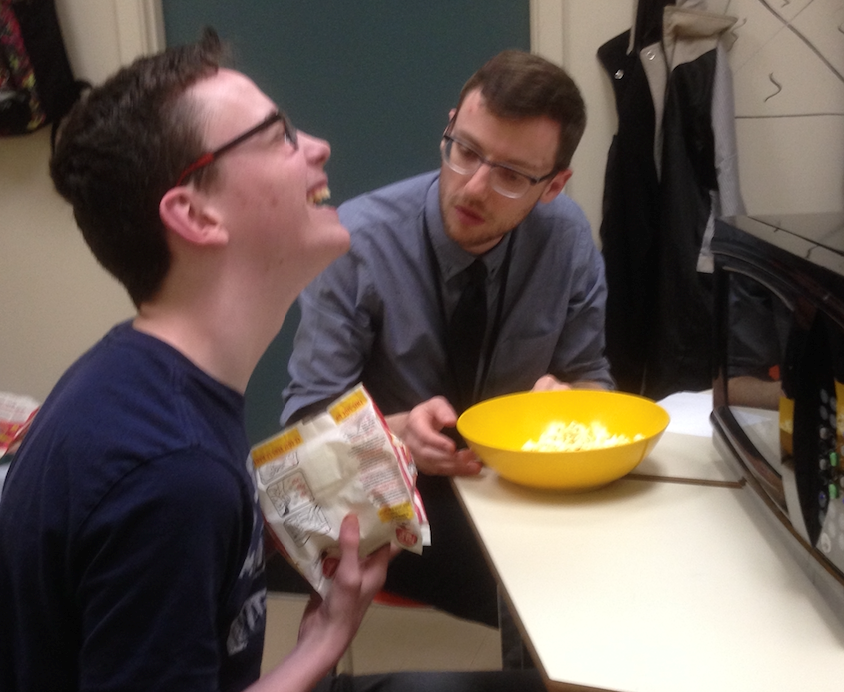 Images shows a student laughing while pouring a bowl of popped popcorn