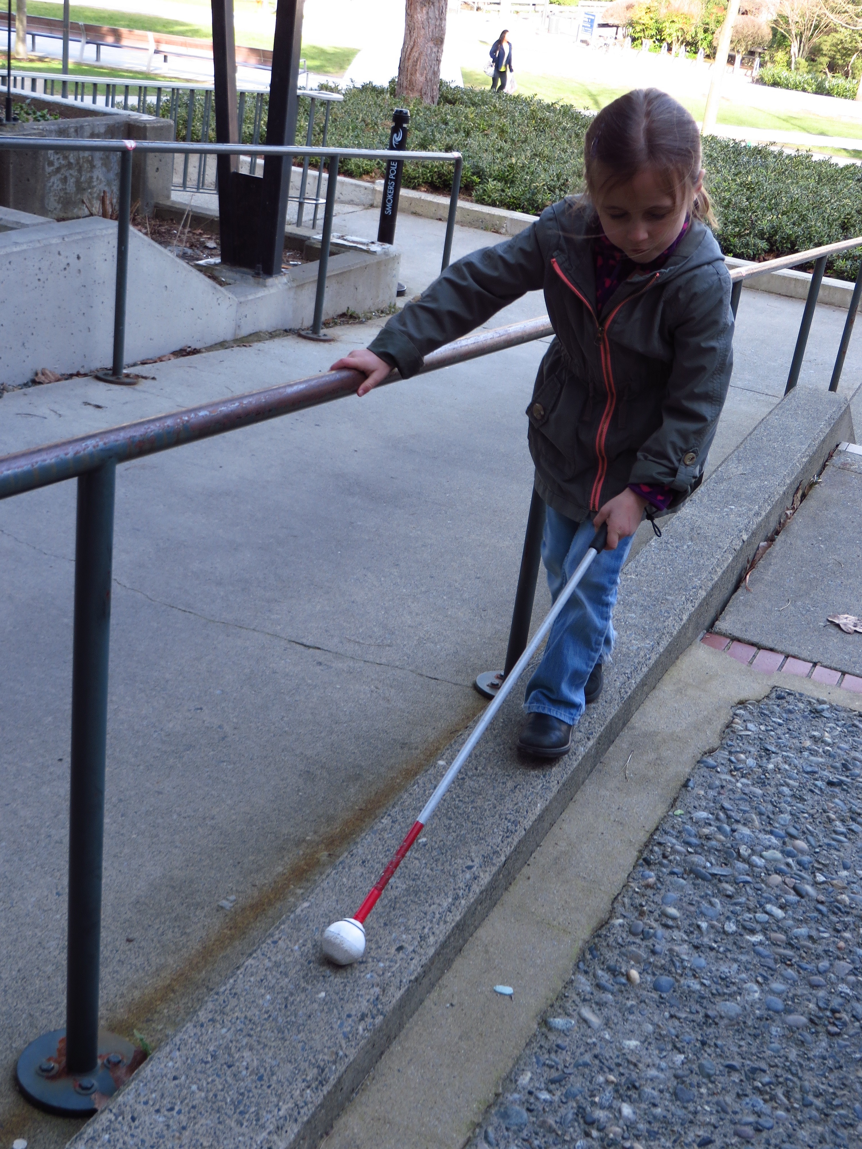 Photos shows a student using a mobility cane to navigate a narrow walkway.