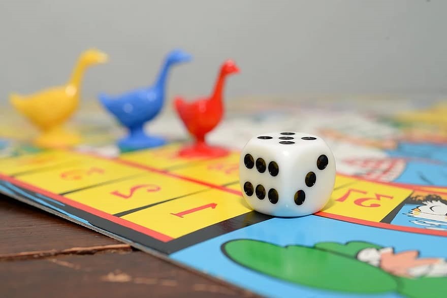Close up photo of a board game board with game pieces shaped like geese and a 6 sided dice.