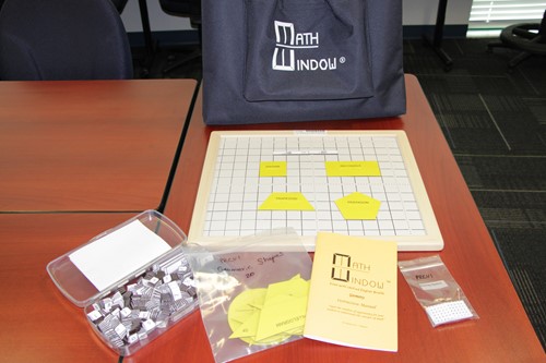 Images shows the contents of the Math Window kit. Shapes tiles are placed on the board in the foreground.
