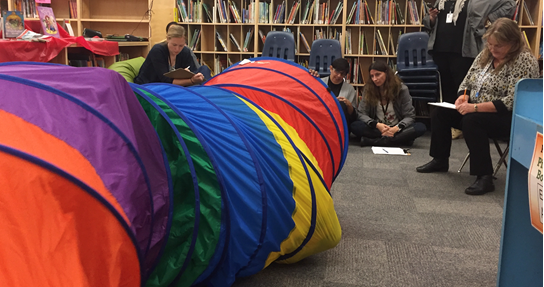 Image shows the TPBVDA team observing a student playing in a multi-coloured play tunnel.