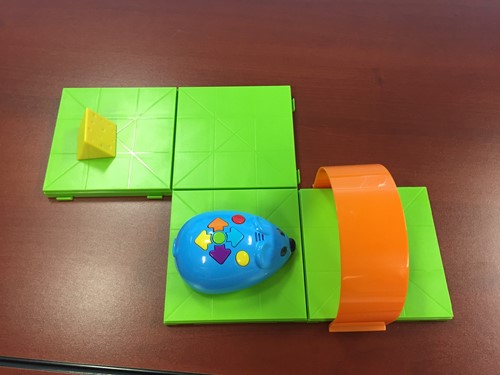 Photo shows a programmable robot mouse on a track made of interlocking plastic squares. A target plastic piece of cheese sits nearby.