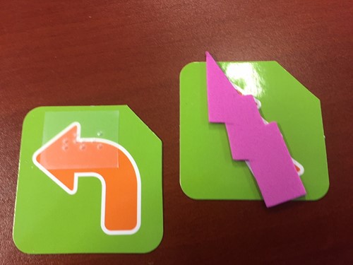 Photo shows two game pieces. A left turn arrow with a braille label and a special card with a tactile jagged shape