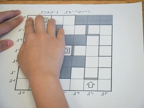 Photo shows a student's hands exploring the tactile diagram of the Swift Playground grid.
