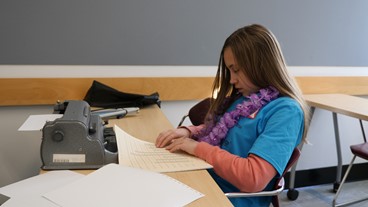 A student wearing a flower lei explores a tactile bar graph at the Braille Challenge
